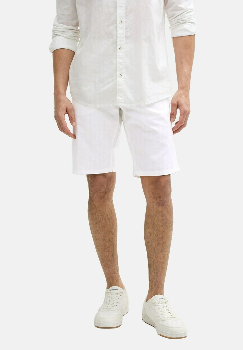 Weiße Baumwollshorts mit geradem Schnitt und seitlichen Taschen, kombiniert mit einem passenden weißen Langarmshirt. Getragen mit weißen Sneakers.
