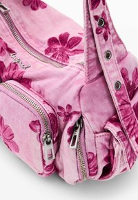Lyserød stofhåndtaske med mørk lyserødt blomsterprint, to sølv lynlåse og en justerbar rem med metaløjer.
