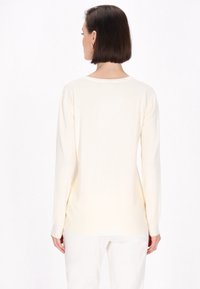 Cremfarbener Pullover mit langen Ärmeln, rundem Ausschnitt und gerippten Bündchen. Der Stoff wirkt weich und glatt mit minimalen Designdetails.