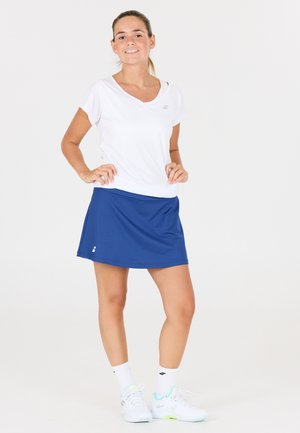 Hvid atletisk T-shirt med korte ærmer og V-hals, parret med en blå sporty nederdel. Har logo-detaljer og tekstureret stof.