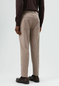 Beige broeken van gladde stof, met rechte pijpen, twee achterzakken, gecombineerd met donkerbruine loafers.