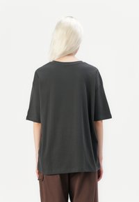 Mørk grå, oversized t-skjorte laget av bomull; har en klassisk rund hals og korte ermer. Glatt tekstur med en avslappet passform.