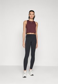Maroon crop top with a Nike logo, paired with fitted black leggings. Model wears white athletic shoes. Simple, clean design.