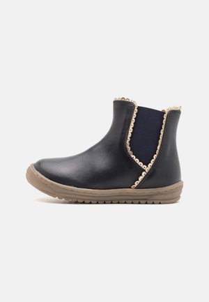 Bottine en cuir noir avec un panneau élastique bleu marine, un bord décoratif festonné et une semelle en caoutchouc texturée. Bout rond et design plat.