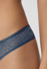 Dunkelblaue Spitzenunterwäsche mit floralen Mustern, gewellten Kanten und einer sanften Textur. Sichtbares Detail des elastischen Taillenbands.