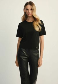Czarny t-shirt z krótkim rękawem i okrągłym dekoltem, wykonany z miękkiego materiału. W połączeniu z czarnymi skórzanymi spodniami z kanciastymi szwami.