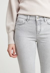 Jasnoszare dżinsy wykonane z denimu, o dopasowanym kroju, z przednimi kieszeniami, suwakiem oraz metalowymi guzikami.