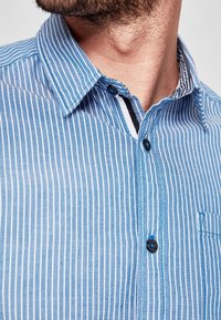 Blauw-wit gestreepte korte mouwen shirt met zwarte knopen, een kraag en een kleine borstzak met contrasterende stofdetails.