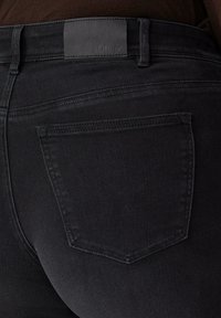 Czarne dżinsy z denimu o gładkiej fakturze, wyposażone w małą tylną kieszeń oraz prostokątną skórzaną naszywkę z napisem "s.Oliver" na talii.