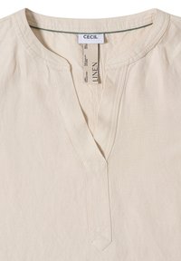 Chemise en lin beige avec un col rond et une courte patte de boutonnage, avec une étiquette de marque « CECIL » et une étiquette en tissu à l'intérieur du col.