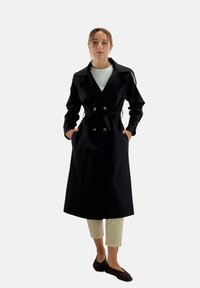 Zwarte trenchcoat met dubbele rij knopen, brede kraag en riem, voorzien van zijzakken en een gladde, gestructureerde stof.