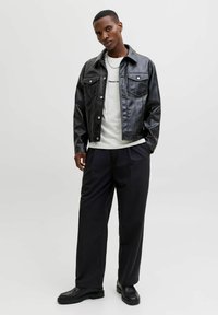 Mustmust värvi kunstnahast jakk nööpidega esiosas, kahe rinnataskuga ja kaelusega. Stiliseeritud heledat halli T-särki kandes koos mustade pükstega.