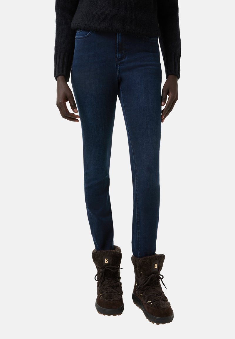 Modré džíny skinny z denimu s hladkým povrchem a klasickým designem pěti kapes, spárované s tmavohnědými botami podšitými kožešinou, které mají šněrování a zlaté detaily.