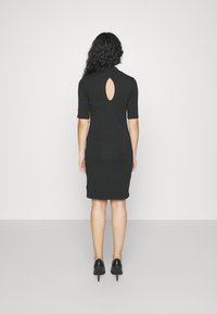 Svart figursydd klänning med nyckelhålsdesign bak, korta ärmar, knä-lång nederkant och slät textur. Bärs med svarta klackar.