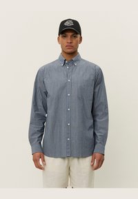 Striped button-up shirt in blue and grey tones, cotton fabric, long sleeves, single chest pocket, and standard collar. Paired with light shorts.