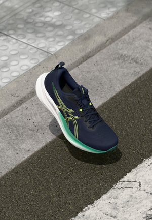 Navy athletic shoe with a textured upper, green accents, and a white sole; features a reinforced toe and a pull tab on the heel.