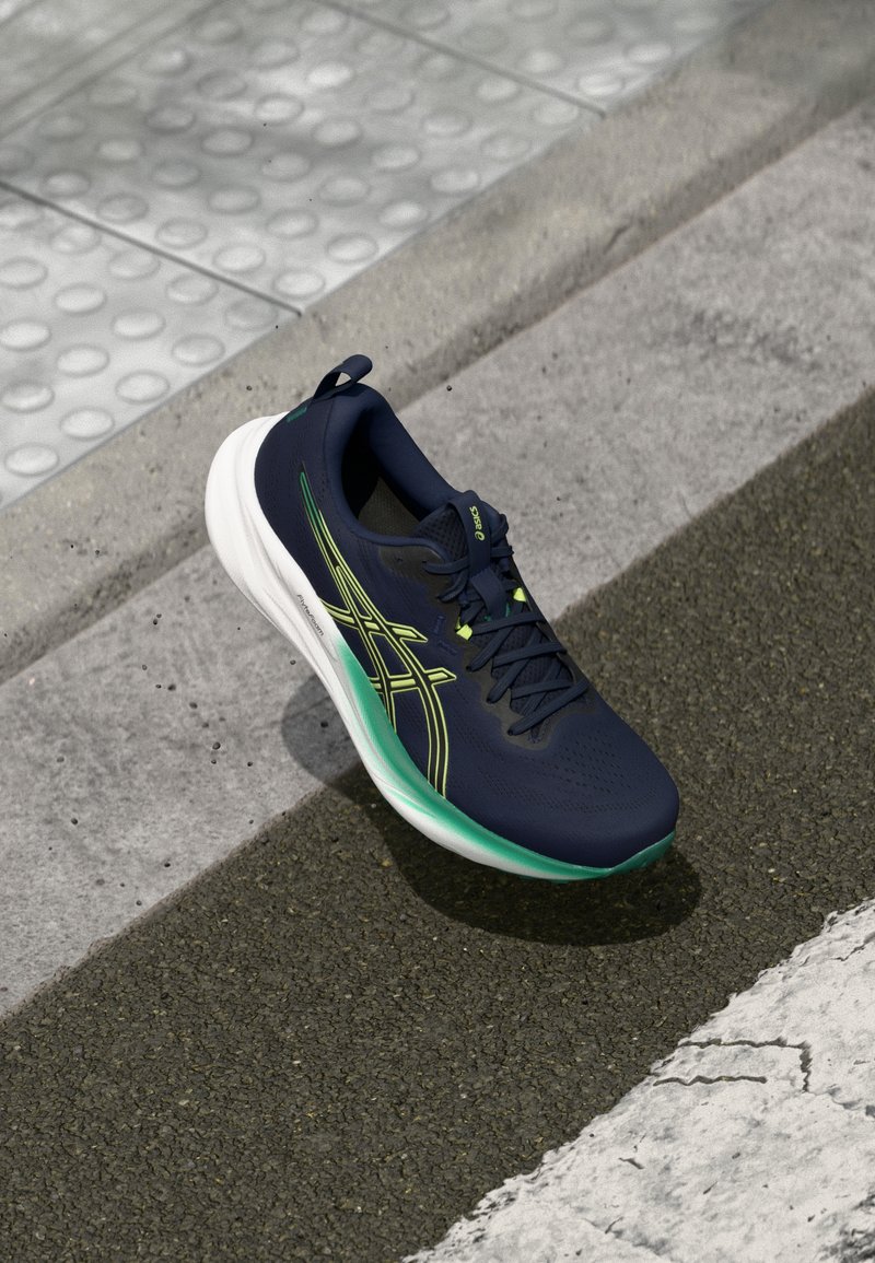 Marineblauw sportshoe met een gestructureerde bovenkant, groene accenten en een witte zool; heeft een verstevigde teen en een trekhaak aan de hiel.