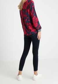 Floral print top in deep navy with bold pink flowers, paired with dark skinny jeans and white sneakers. Long sleeves and striped cuffs.