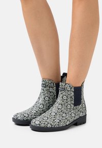 Botas de tobillo con estampado floral en blanco y negro, de material de goma, con paneles laterales elásticos y una suela negra texturizada.