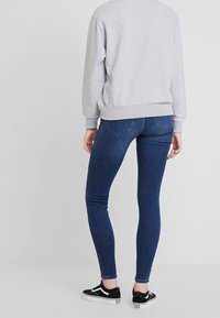 Sudadera gris con puños acanalados, combinada con jeans skinny de color azul oscuro. Zapatillas negras con acentos en blanco. Vista desde la parte de atrás.