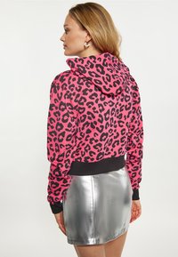 Felpa con stampa leopardata rosa, con orlo e polsini neri, abbinata a una mini gonna metallica argento, che mette in risalto uno stile casual e aderente.