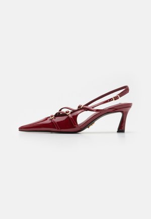 Talons aiguilles en cuir verni rouge avec un bout pointu, des brides fines et des accents décoratifs en or. Talon aiguille modéré.