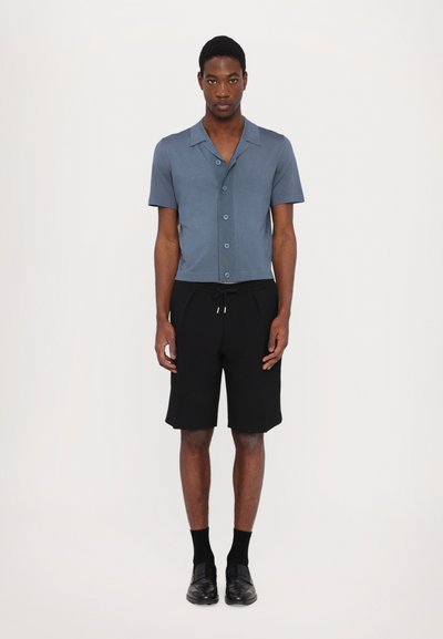 Kortermet skjorte med knapper i lyseblått stoff, kombinert med svarte shorts. Ensemblet har en avslappet passform og klassiske stil detaljer.