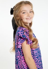 Trumpas rankovės suknelė, kuri turi mėlyną foną su rožiniu leopardų raštu, raukšlėtos rankovės ir didelė juoda juostelė plaukuose.