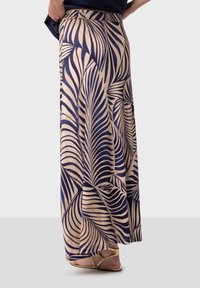 Maxikjol i beige tyg med marinblå lövmönster. Utsvängd design med en mjuk textur och bred midja. Bärs med platta guldiga sandaler.