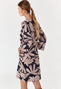 Fließendes knielanges Kleid mit dunkelblauem Hintergrund und großen beigen Blumenmustern, langen Ärmeln und tailliertem Bund.