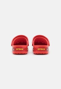 Red plastic clogs with a vented design, featuring a back strap and a textured sole. The word "crocs" is printed in yellow on the heel.