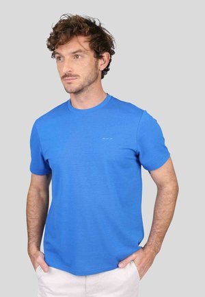 T-shirt bleu à manches courtes, fabriqué en tissu doux, avec un col rond et un discret logo sur la poitrine. Texture lisse.