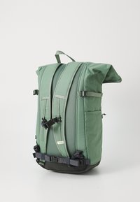 Zaino verde a rullo con spallacci imbottiti, dettagli in rete, fibbie regolabili e una base resistente. Presenta tasche laterali per lo stoccaggio.