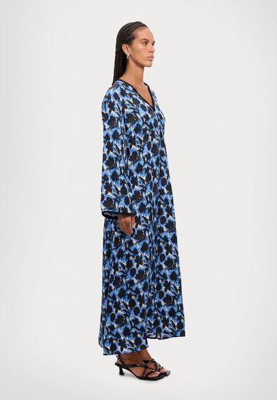 Rochie lungă de culoare albastră cu un model floral în nuanțe de negru și albastru, având mâneci lungi și decolteu în formă de V. Pur însoțită de sandale cu toc subțire de culoare neagră.