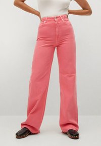 Jean rose à jambes larges avec une taille haute, doté d'une fermeture par bouton et fermeture éclair, de poches avant et d'un ourlet légèrement effiloché. Associé à des sabots noirs.