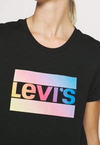 Musta puuvillat-paita, jossa on värikäs graadientti Levi's -logo edessä. Lyhyet hihat ja klassinen pyöreä kaula-aukko.
