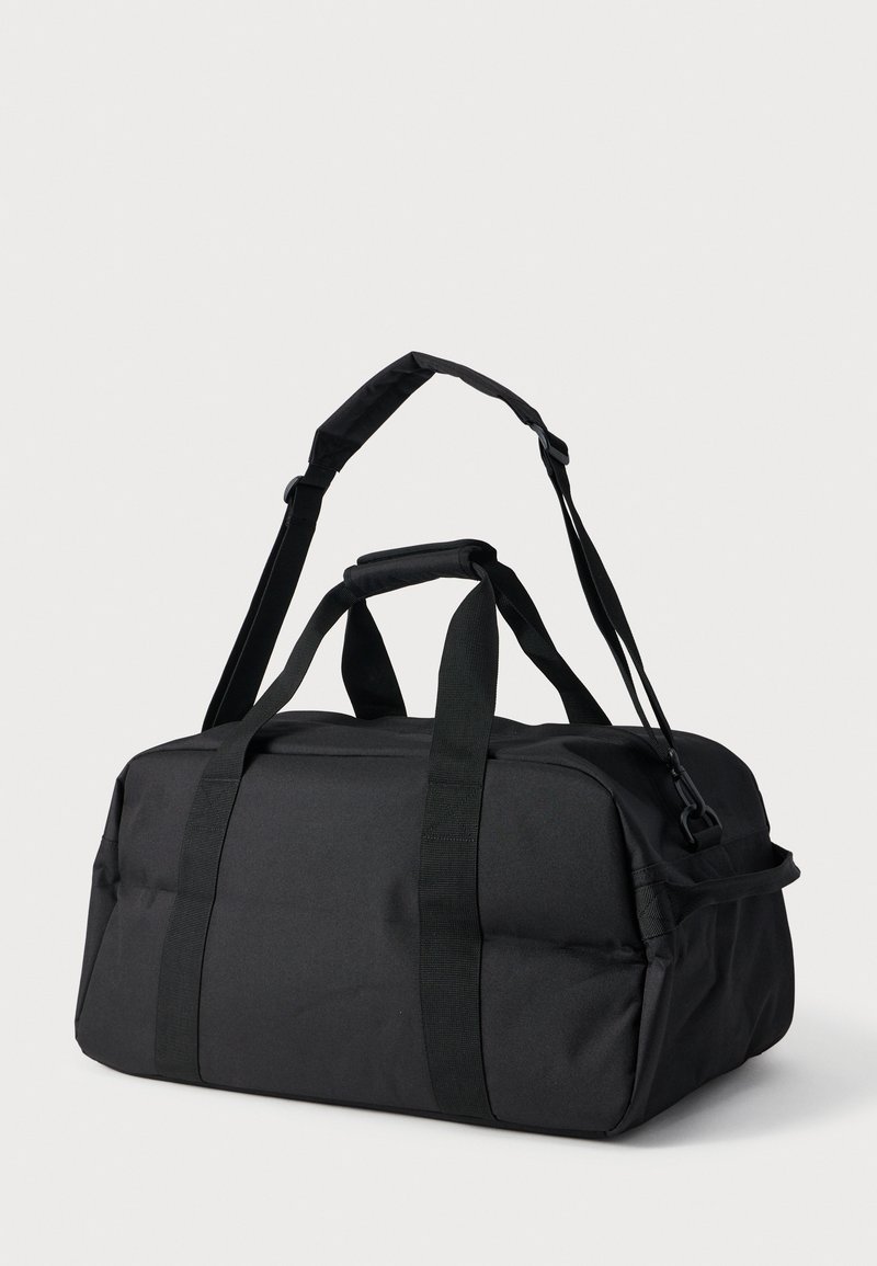 Zwarte rechthoekige duffeltas met dubbele draaghandvatten en verstelbare schouderriem, geplaatst tegen een effen lichte achtergrond.