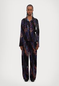 Két részes öltözet, amely egy hosszú ujjú ingből és bő szárú nadrágból áll, egy texturált anyagból készült, fekete alapszínnel és sokszínű absztrakt mintákkal.