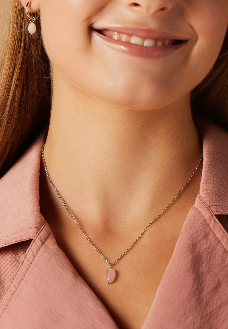 Collier en chaîne argentée avec un pendentif en pierre précieuse rose arrondie. Les boucles d'oreilles comportent une perle rose douce assortie sur un anneau en argent.