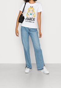 Valkoinen puuvillapaita, jossa on säätytyttö, jolla on vaaleat hiukset, yhdistettynä vaaleansinihin leveälahkeisiin farkkuihin ja valkoisiin tenniskenkiin.