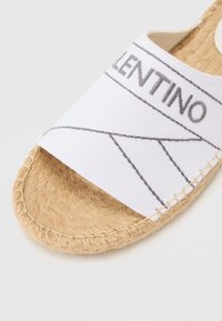 White canvas espadrille slide featuring gray stitched detailing, natural jute sole, and rounded shape. Subtle branding on upper strap.