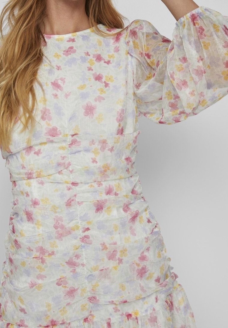 Robe fleurie avec un fond blanc présentant des fleurs roses, jaunes et violettes. Manches bouffantes et détails froncés ajoutent de la texture.