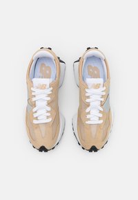 Pár béžových a bílých tenisek New Balance s bílými tkaničkami, síťovinovými a semišovými panely, z pohledu shora na bílém pozadí.