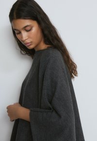 Suéter grande de color gris oscuro con mangas anchas y escote barco, confeccionado con un tejido de punto suave y texturizado. Presenta un ajuste relajado y un diseño minimalista.