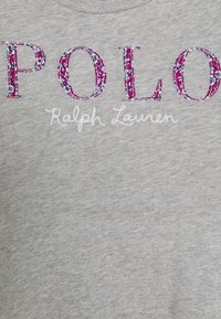 Szary bawełniany t-shirt z napisem "POLO" w różowej, teksturowanej i kwiatowej haftowanej formie, z napisem "Ralph Lauren" poniżej, napisanym białą kursywą.