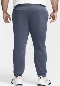 Pantalones jogging azul marino hechos de material suave, con un diseño de pierna ajustada y cintura elástica, combinados con zapatillas deportivas blancas.