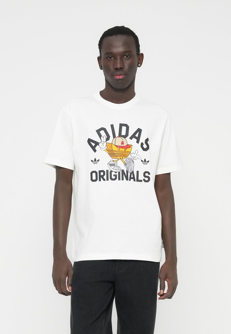 Balti medvilninė marškinėliai su ryškiu grafiniu atspaudu, kuriame yra tekstas „ADIDAS ORIGINALS“ ir animacinis personažas, derinami su tamsiomis džinsais.