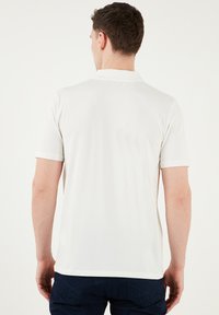 Weißes Kurzarm-Polohemd mit klassischem Kragen, weicher Textur und geradem Schnitt, kombiniert mit dunkelblauen Hosen.