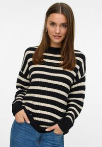 Pruhovaný černobílý pletený svetr s kulatým výst�řihem; má ribbed manžety a lem a má volný střih. Nosený s modrými džíny.