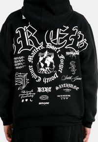 Czarna bluza z kapturem z dużymi białymi napisami i grafikami, w tym globusem oraz różnymi stylizowanymi logo marek na plecach.